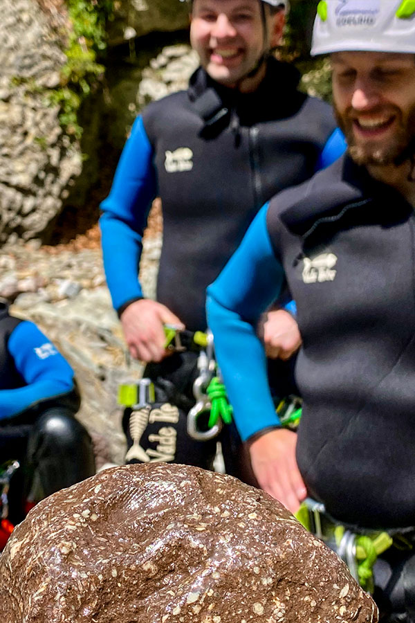 Nummulitenkalk und purelements-Canyoninggruppe in der Starzlachklamm Canyoningteilnehmer in der Starzlachklamm hinter einem Block aus fossilem Nummulitenkalk mit sichtbaren Foraminiferen-Strukturen